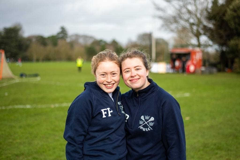 Two female members of the lacrosse team stand side by side smiling