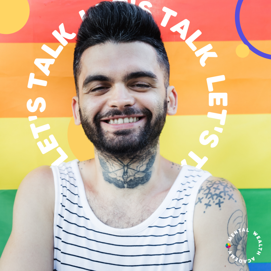 Man with dark hair and vest top smiling in front of rainbow flag with words Let's Talk in curved writing